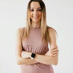 A cheerful young woman standing with arms crossed, exuding confidence and wellness.
